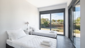 A modern bedroom with two beds, a nightstand, and a large sliding glass door leading to an outdoor area. - Minimal Maisonette In Porto Cheli (Porto Cheli)