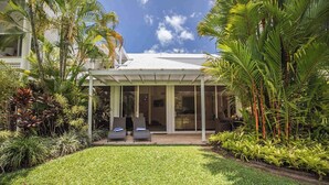 A modern house with a covered patio, two lounge chairs, and lush tropical plants. - Port Douglas Mirage Villa 408 (Port Douglas)