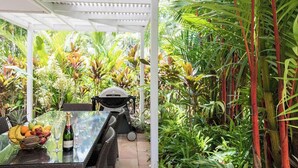 An outdoor patio with a glass table, a grill, and a variety of tropical plants. - Port Douglas Mirage Villa 408 (Port Douglas)