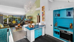 Une cuisine moderne avec un plan de travail bleu, un luminaire suspendu et une vue sur l’extérieur.
