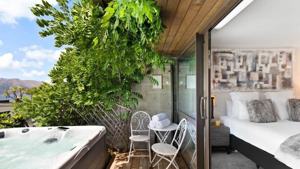 Un balcon doté d’un jacuzzi, de fauteuils en osier et d’un lit offrant une vue sur les montagnes.