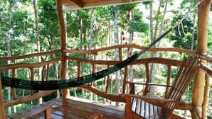 Una terraza de madera con una hamaca, rodeada de árboles.