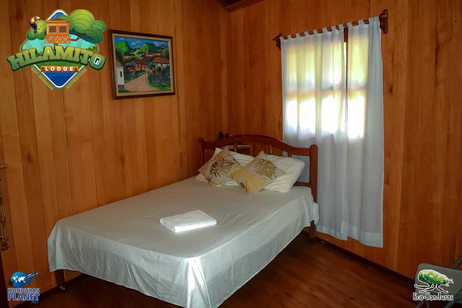 Una stanza in legno con un letto, un quadro e una finestra con tende.