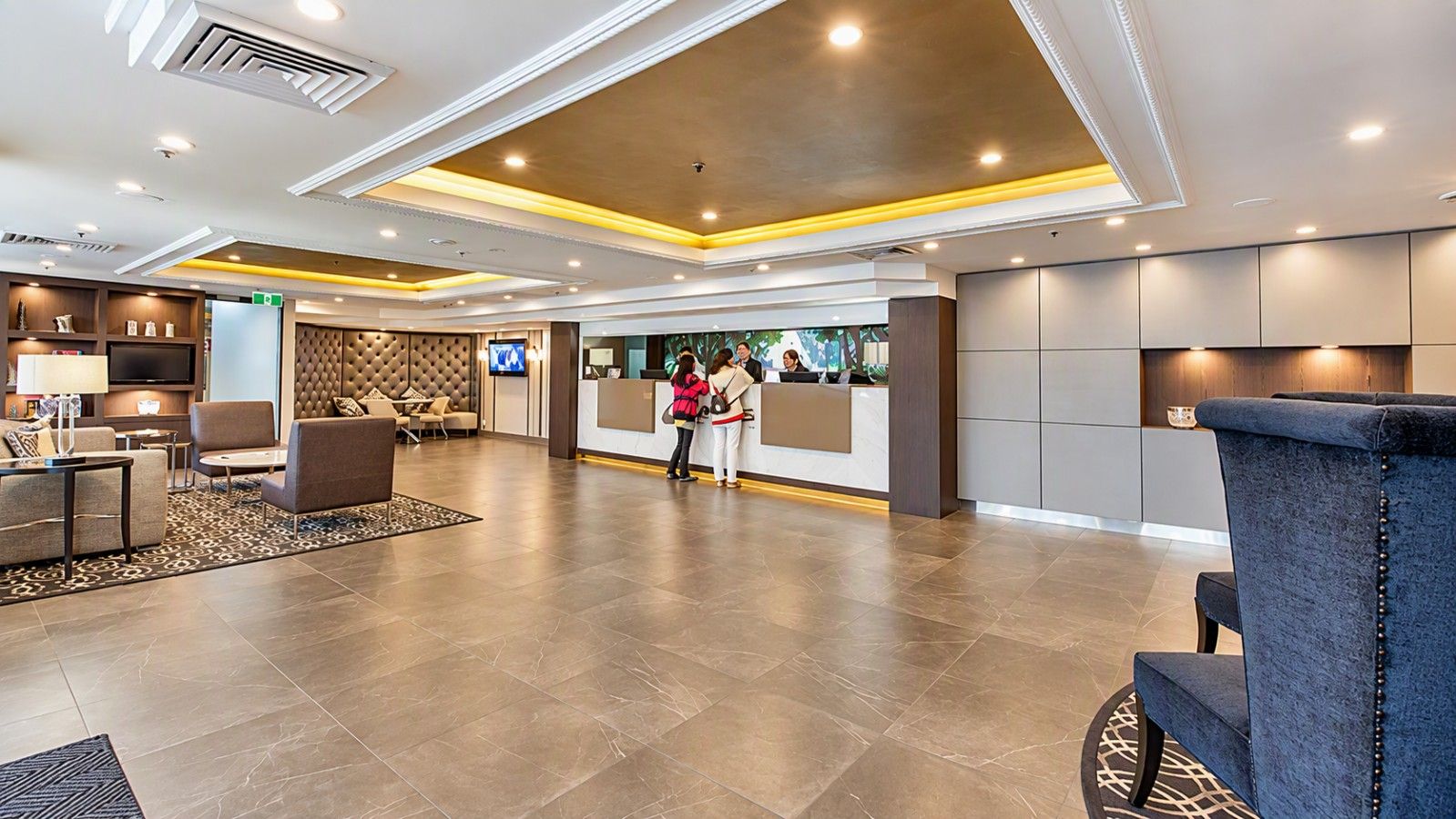 A hotel lobby with a reception desk, seating area, and a television.