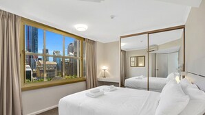 Une chambre d’hôtel avec un grand lit, une table de chevet avec une lampe, une fenêtre avec des rideaux et un miroir.