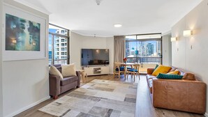 Un salon moderne comprenant un canapé, un téléviseur, un coin repas et un balcon offrant une vue sur la ville.