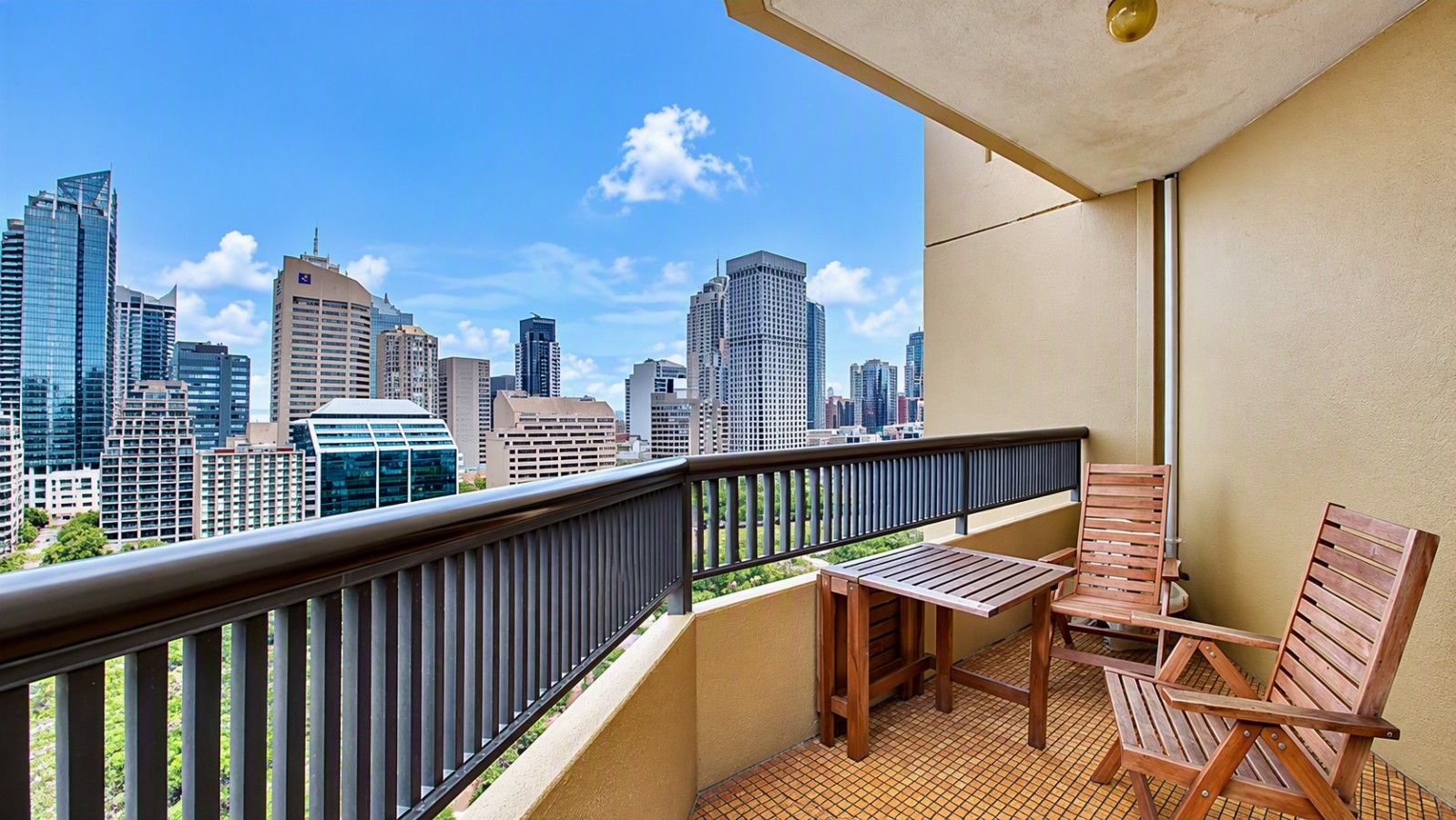 A balcony with a view of a city skyline, a table, and two wooden chairs.