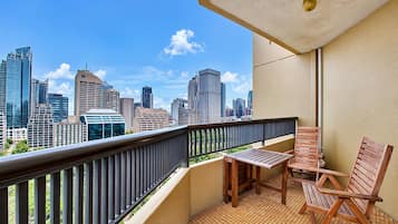 A balcony with a view of a city skyline, a table, and two wooden chairs.
