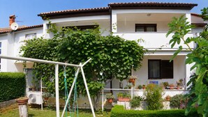 A house with a white exterior, a garden with a swing set, and potted plants. - Spacious holiday apartment, only 1km from the beach (Valbandon, Fažana)