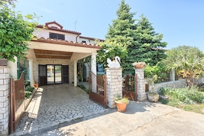 Ein Haus mit einem gepflasterten Eingangsbereich, einer Veranda und einer befestigten Auffahrt.