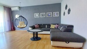 A modern living room with a sectional sofa, a hanging chair, and a small round table. - Spacious holiday apartment, only 1km from the beach (Valbandon, Fažana)