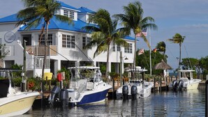 A waterfront property with a docked boat, a guest house, and palm trees. - Oceanfront, 2 Bedroom Unit At Ocean Pointe Condominium (Tavernier)