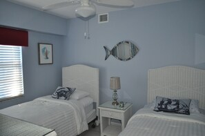 A bedroom with two beds, a ceiling fan, a bedside table with a lamp, and a wall-mounted fish mirror. - Oceanfront, 2 Bedroom Unit At Ocean Pointe Condominium (Tavernier)
