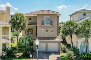 A multi-story residential building with a garage, surrounded by palm trees and a well-maintained lawn.