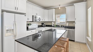 Een moderne keuken met witte kasten, een zwart granieten aanrechtblad en een vast eiland met barstoelen.