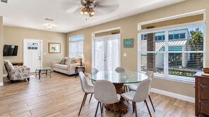 A spacious living room with a glass dining table, comfortable seating, a television, and a view of the outdoors through large windows. - Oceanic View |  720FT walk to private beach access | FREE Golf Cart (Destin)