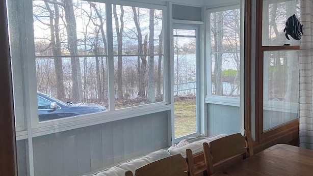 A dining area with a large wooden table and benches, large windows with a view of trees and a body of water.
