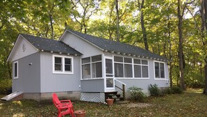A small, single-story house with a porch, surrounded by trees and covered in fallen leaves.