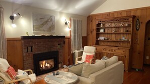 A cozy living room with a brick fireplace, wooden shelves, and a comfortable sofa.