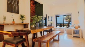 A modern living room with a wooden dining table, benches, and a sofa. There are potted plants and a large window with a view. - VILLA ISLA MUJERES MAYAKITA, FANTASTIC OCEAN VIEW & ROOFTOP (Meteorológico)