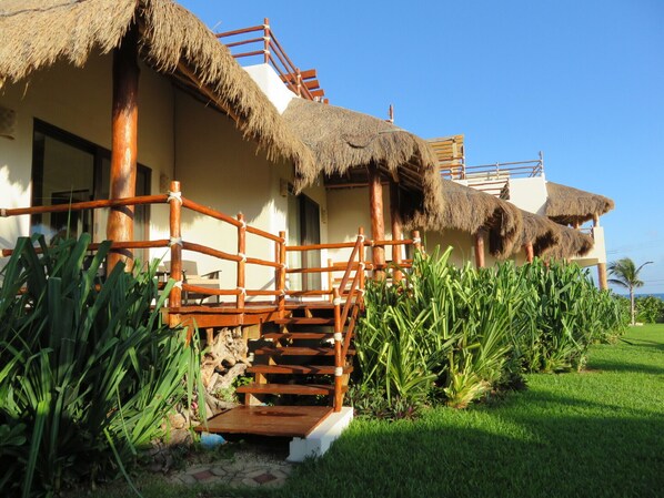 A resort with a thatched-roof building, wooden staircase, and lush greenery.