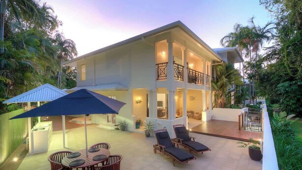 A two-story house with a balcony, outdoor seating area, and a well-lit patio.