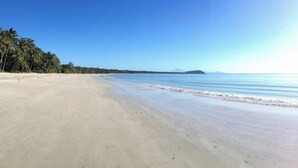 A beach with clear skies, calm waters, and a distant mountain.