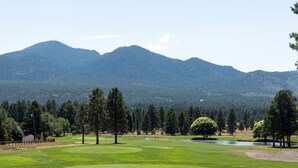 Un parcours de golf avec un étang, des arbres et des montagnes en arrière-plan.
