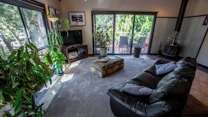 Una sala moderna con un sofá de cuero, una mesa de centro y un televisor. Hay plantas en macetas y un ventanal corredero que da a un área exterior.