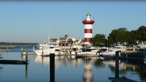 A marina with boats docked, a lighthouse, and a building with a red and white striped tower. - July 4th Week MARRIOTT'S HARBOUR CLUB AT HARBOUR TOWN excellent location in town (Hilton Head Island)