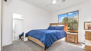 A bedroom with a bed, a nightstand, a wooden dresser, a ceiling fan, and a window with a view of trees. - Regent Retreat - Sleeps 15, BBQ, pool (Moama)