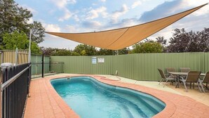 A rectangular swimming pool with a brick border, surrounded by a green fence and a shaded area. - Regent Retreat - Sleeps 15, BBQ, pool (Moama)