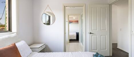 A bedroom with a bed, a nightstand, a round mirror, and a door leading to another room.
