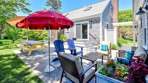 A patio with outdoor furniture, a red umbrella, and a garden area with flowers. - Central AC Close to Beach Dog Friendly! (Chatham)