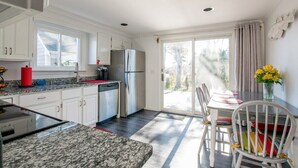 A kitchen with white cabinets, a stainless steel refrigerator, a granite countertop, and a dining area with a table and chairs. - Central AC Close to Beach Dog Friendly! (Chatham)