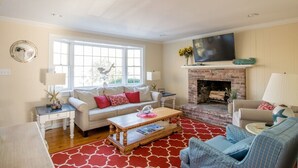 A living room with a fireplace, a sofa, a coffee table, and a television. - Central AC Close to Beach Dog Friendly! (Chatham)