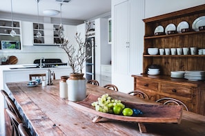 A wooden dining table with a fruit centerpiece, white cabinets, and a wooden sideboard with dishes. - Forest View., Stunning HIA Building Award Winner, luxuriously appointed and comfortable. Perfect for... (Castlemaine)