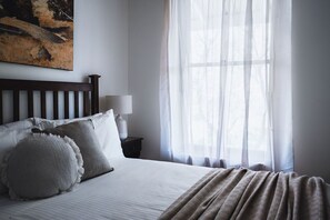 A neatly made bed with pillows, a bedside lamp, and a window with sheer curtains. - Forest View., Stunning HIA Building Award Winner, luxuriously appointed and comfortable. Perfect for... (Castlemaine)