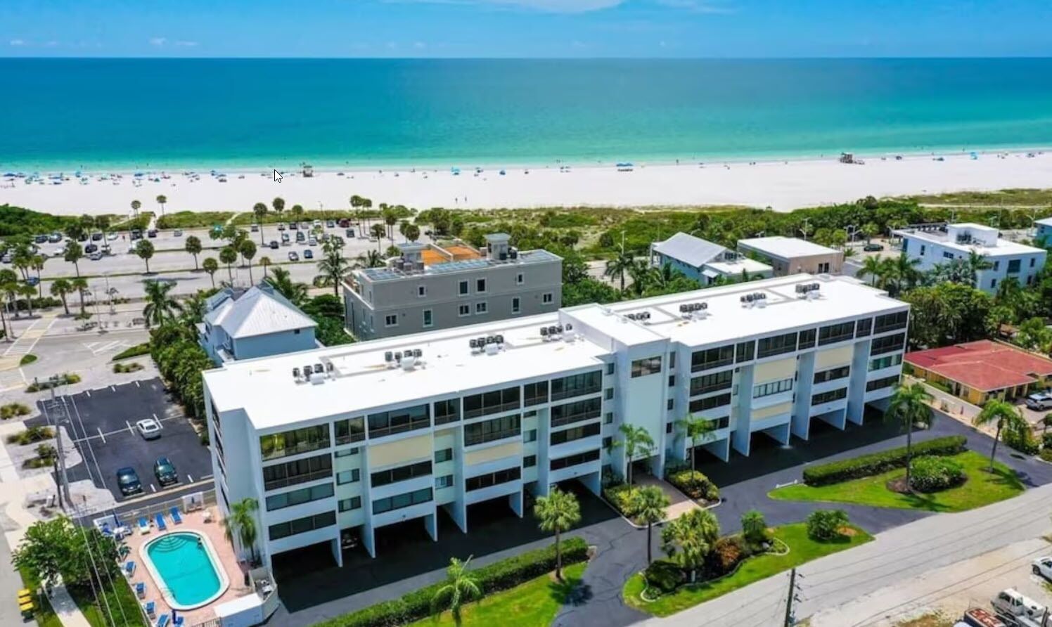 An aerial view of a hotel with a pool, a beach, and a parking lot.