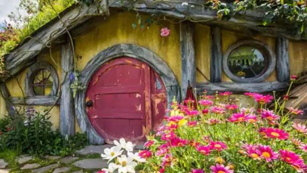 A Hobbit-style house with a red door, round windows, and a garden with colorful flowers.