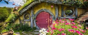 A Hobbit-style house with a red door, round windows, and a garden with colorful flowers. -  GREENCROFT -  STAY, PLAY AND GET AWAY (Aongatete)