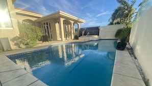 A swimming pool with a clear blue water surface, surrounded by a tiled deck and a building with a modern architectural style in the background.
