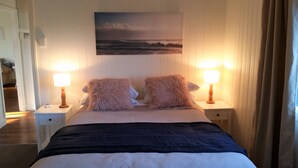 En seng med to bløde puder, et sengebord med en lampe, og et maleri af et landskab på væggen.