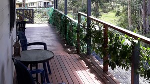 Eine Holzterrasse mit Tisch und Stühlen, ein überdachter Bereich mit Blick auf ein Haus und Bäume.