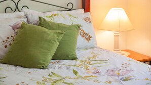 Ein Bett mit floralem Bettzeug und zwei grünen Kissen, eine Nachttischlampe und ein Holznachttisch.