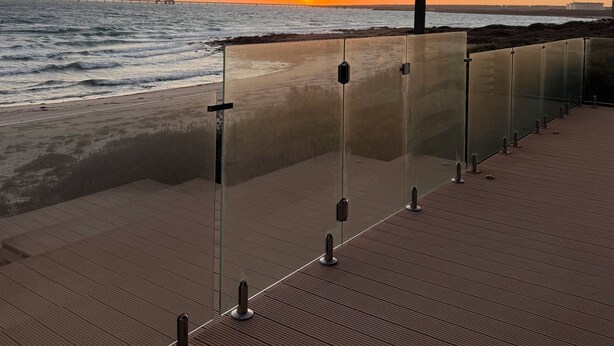 A wooden deck with glass railings overlooking a beach at sunset.