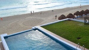 A swimming pool adjacent to a beach with a grassy area and thatched umbrellas. - Casa Pelicano by B&G - Beach Front Villa Cancún Hotel Zone (Cancún)