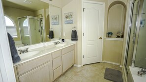 A bathroom with two sinks, a large mirror, a shower, and a door.