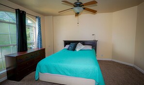 A bedroom with a bed, a dresser, a ceiling fan, and a window with curtains.