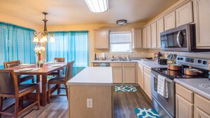A modern kitchen with wooden cabinets, a central island, stainless steel appliances, and a dining area with blue curtains. - A Bit of Country, All the Perks of the City (Helotes)